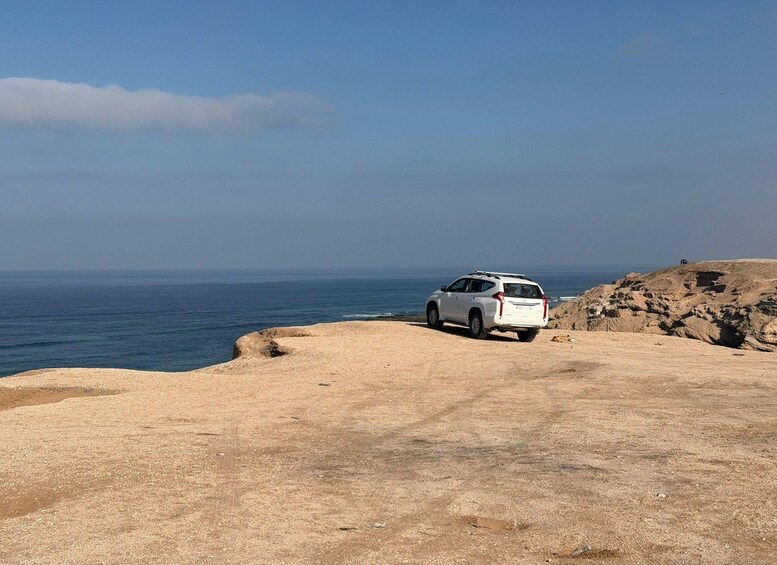 Un VUS blanc est garé sur une plage rocheuse, avec l’océan en arrière-plan. 2