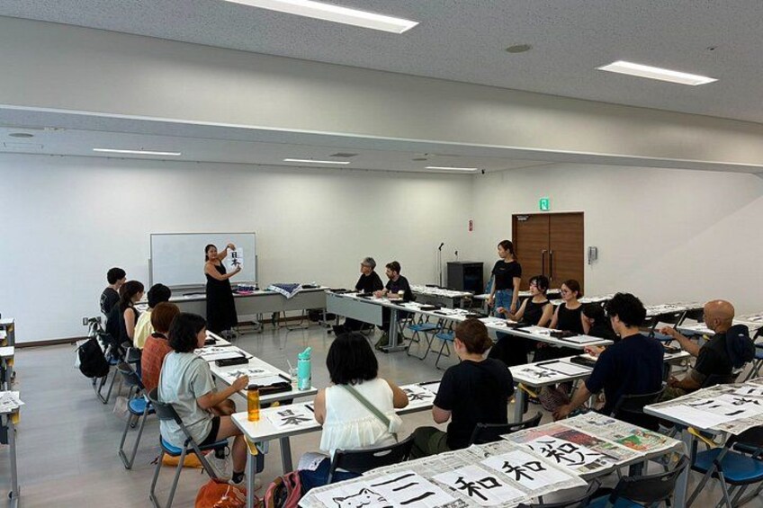 A classroom with students seated at desks, a teacher standing at the front, and a whiteboard. 4