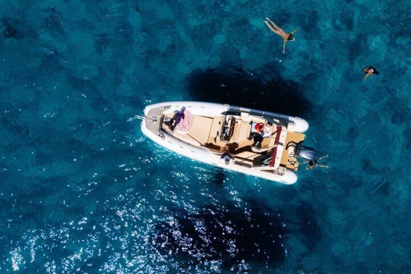 A boat on clear blue water with people on board and two divers swimming nearby. 3