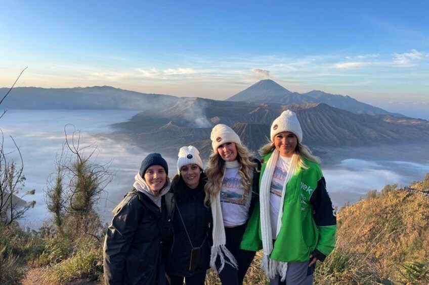 A group of people on a mountain with a view of a volcano and clouds below. 1