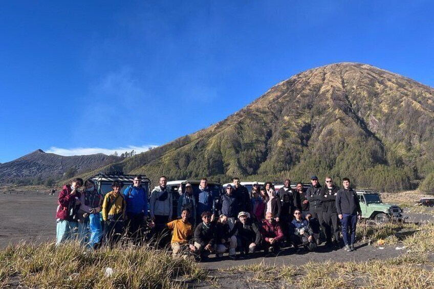 A group of people gathered around a vehicle in a natural landscape with a mountain in the background. 4