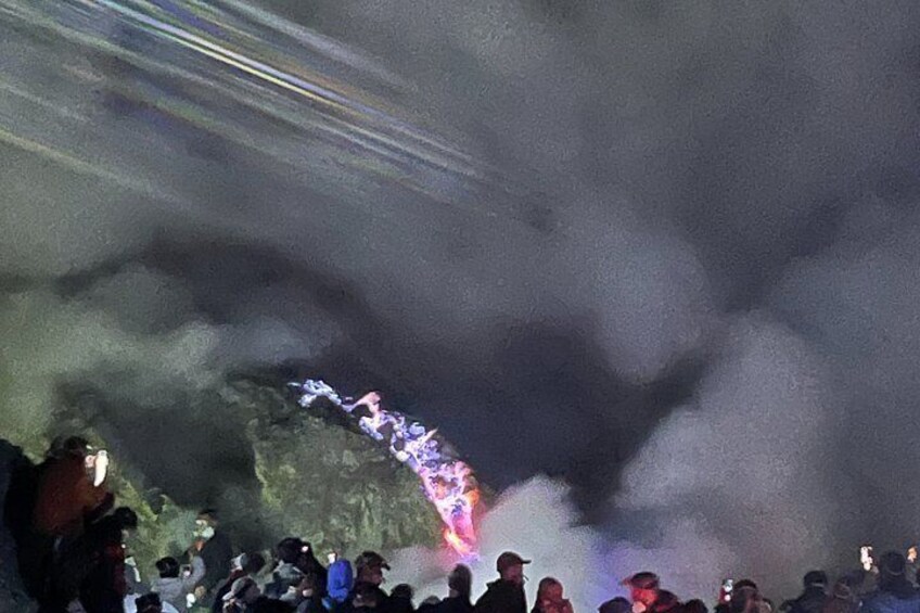 A crowd of people gathered around a rocky area with smoke or fog. 2