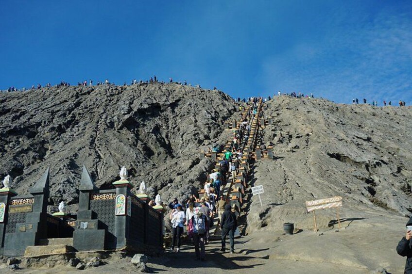 A steep, rocky mountain with a long line of people ascending. 2