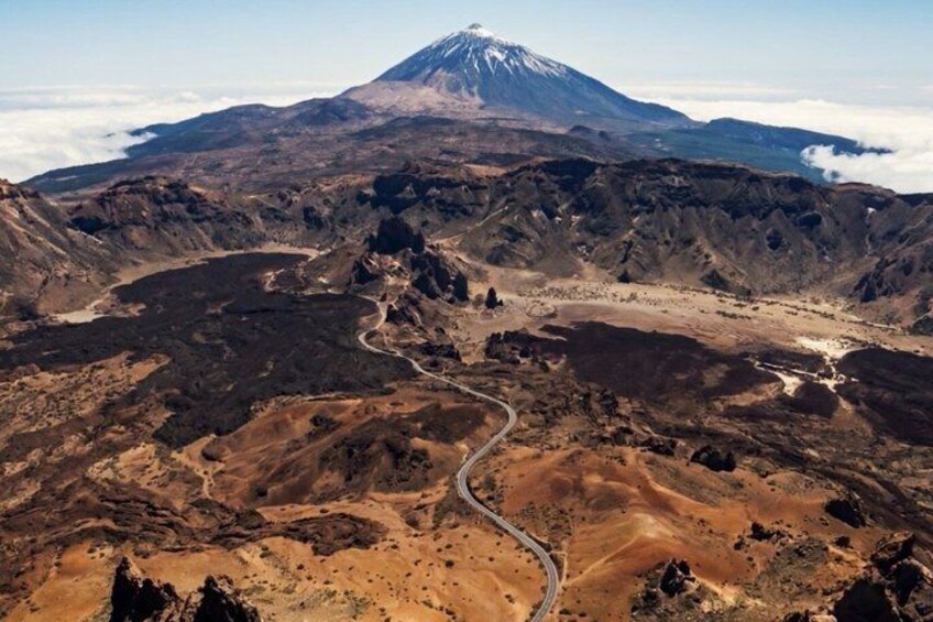 A volcanic landscape with a winding road and a snow-capped mountain in the background. 3