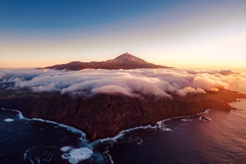 A mountain with a snow-capped peak, surrounded by clouds, and a coastline with waves. 5