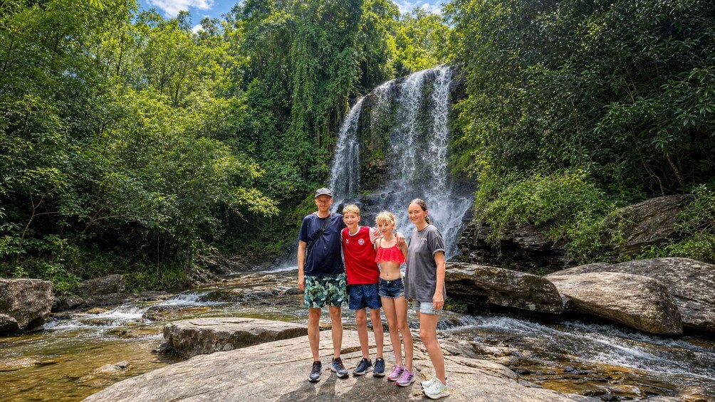 A family standing on a rock by a waterfall in a forested area. 3
