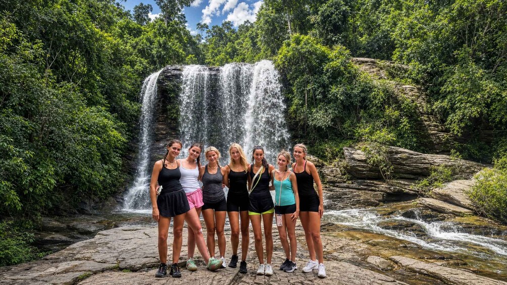 A group of people standing in front of a waterfall surrounded by lush greenery. 5