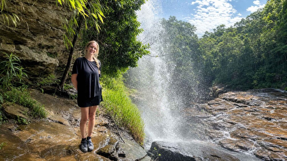 A waterfall in a forested area with a person standing on a rock. 2
