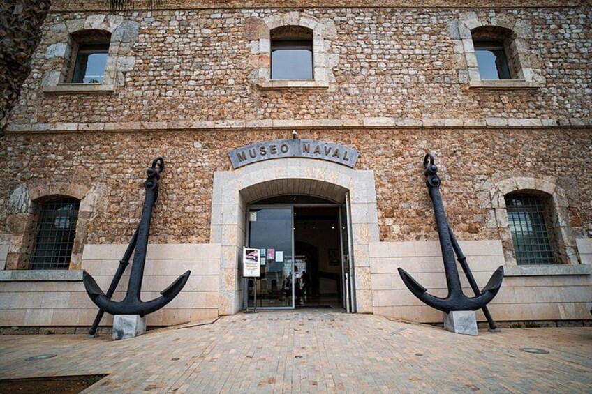 A stone building with a sign reading 'Museo Naval' and two large anchors in front. 2