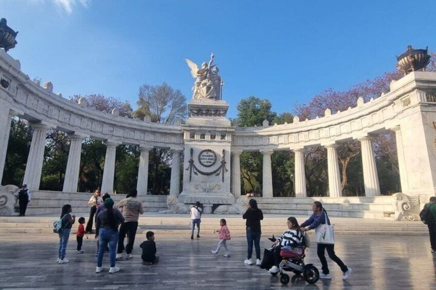 A large open plaza with a central monument surrounded by columns, people walking, and a statue on top. 4