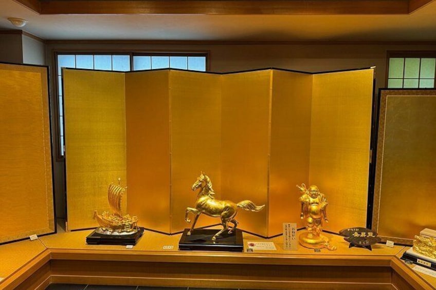 A display of golden artifacts, including a horse and a figure, on a table with a backdrop of a golden partition. 3