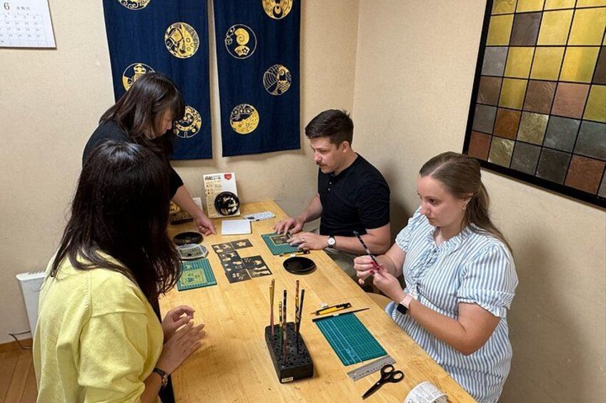 Four people at a table with crafting materials, including scissors, rulers, and a cutting mat. 3