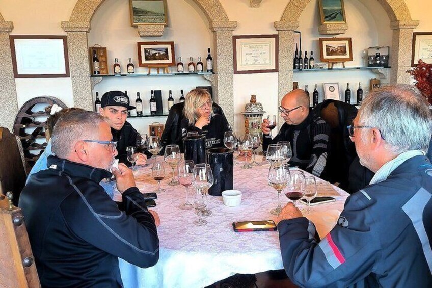 A group of people seated at a table with wine glasses, surrounded by shelves of wine bottles. 1
