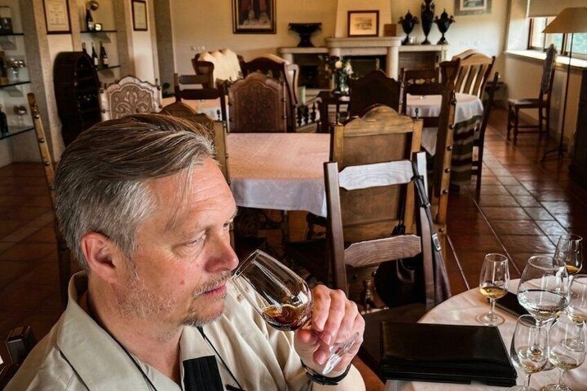 A man seated at a table in a dining area with wooden chairs and a white tablecloth. 5