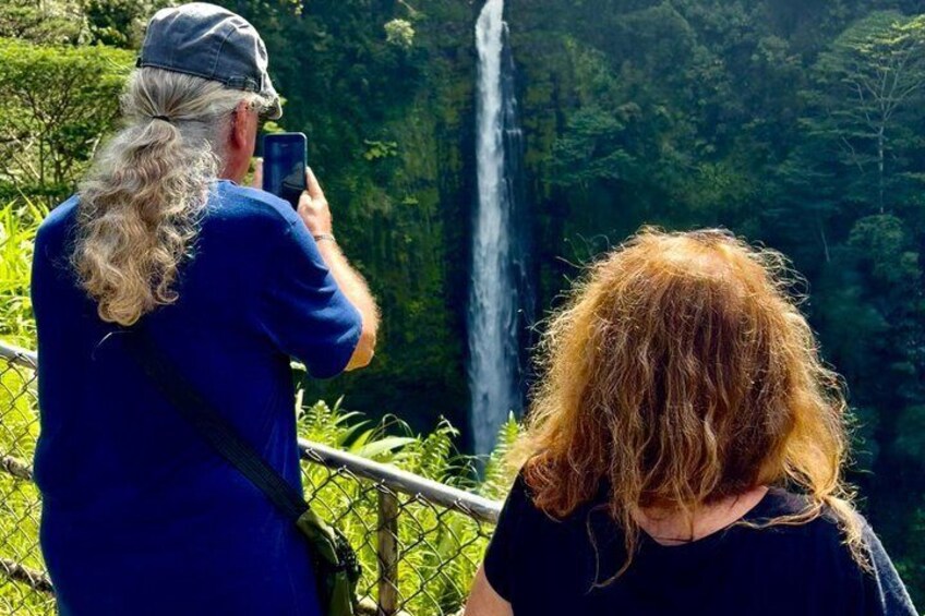 A person taking a photo of a waterfall with lush greenery in the background. 5