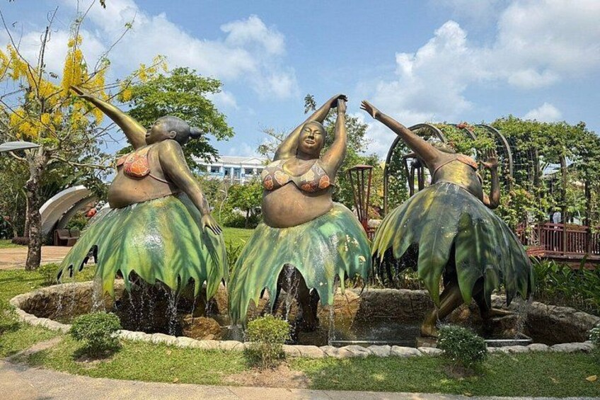 A statue of a woman in a bikini with a leaf skirt, standing in a garden with a fountain. 2