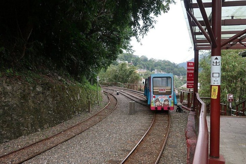 A train on tracks with a station platform and trees in the background. 3