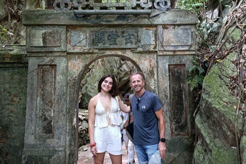 A stone archway with inscriptions, a person in a white outfit, and another in a blue shirt. 3