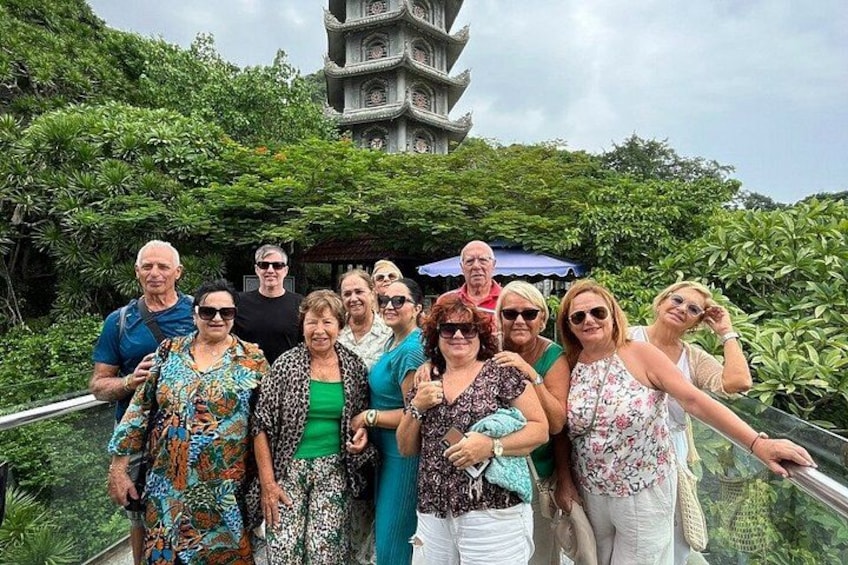 A group of people posing in front of a pagoda-style structure surrounded by lush greenery. 1
