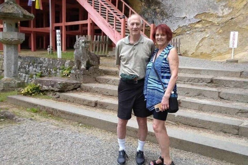 A man and woman standing in front of a stone lion statue, with a staircase and a building in the background. 5