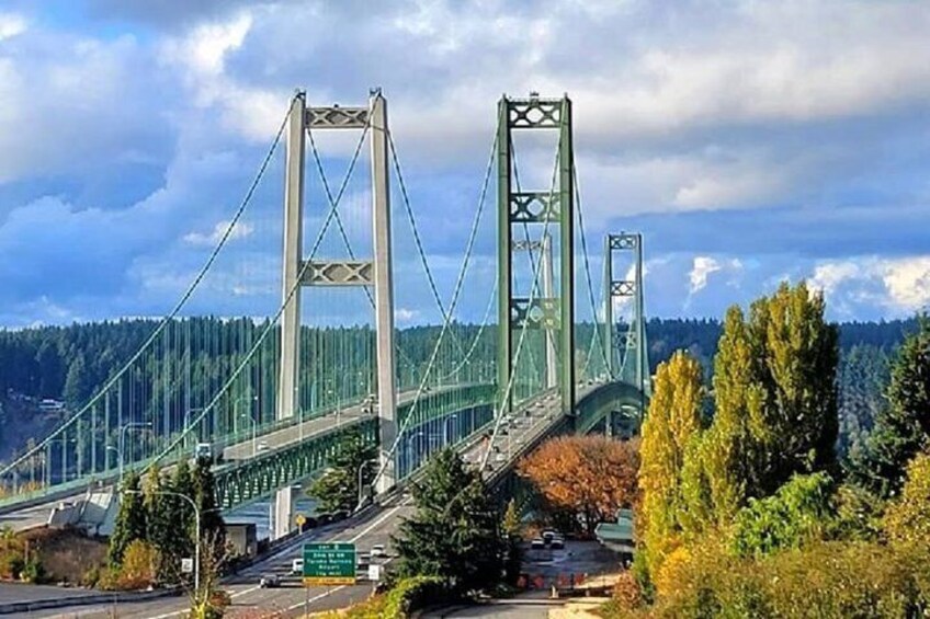 A large suspension bridge with two towers, surrounded by trees and a cloudy sky. 4