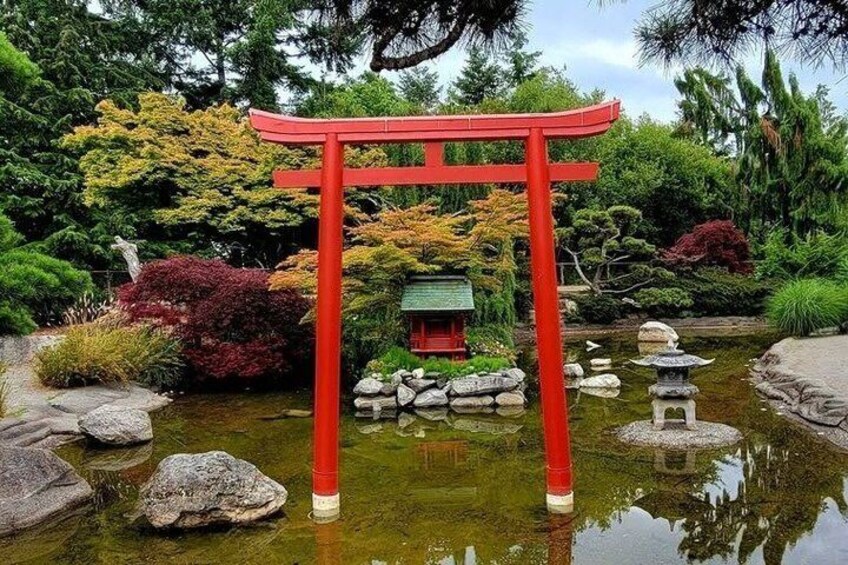 A red torii gate in a Japanese garden with a pond, rocks, and various trees. 3