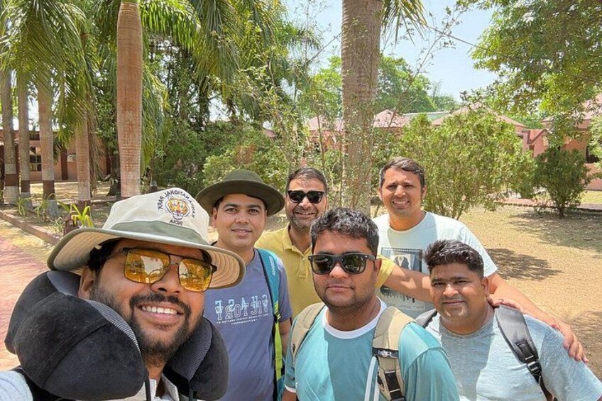 A group of people outdoors, some wearing hats, with palm trees and a building in the background. 1