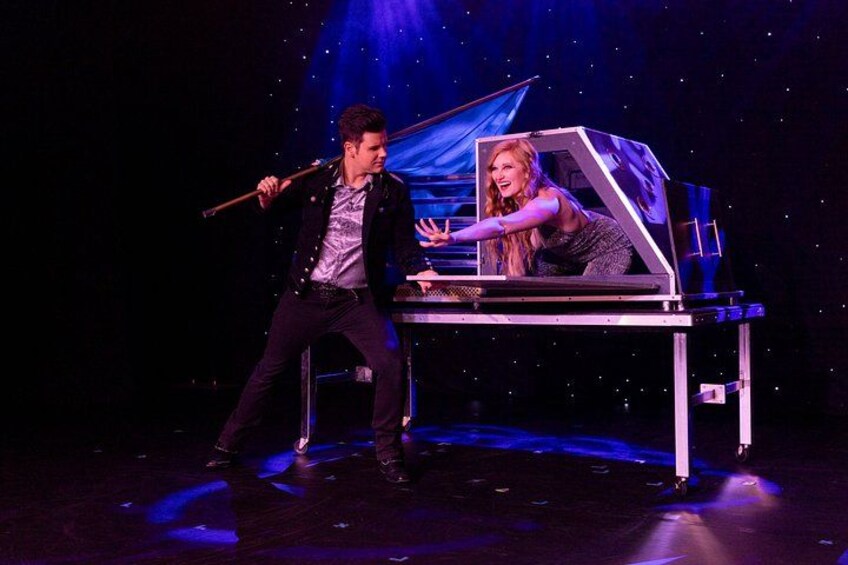 A stage with a piano, a person playing the piano, and another person standing beside it. 3