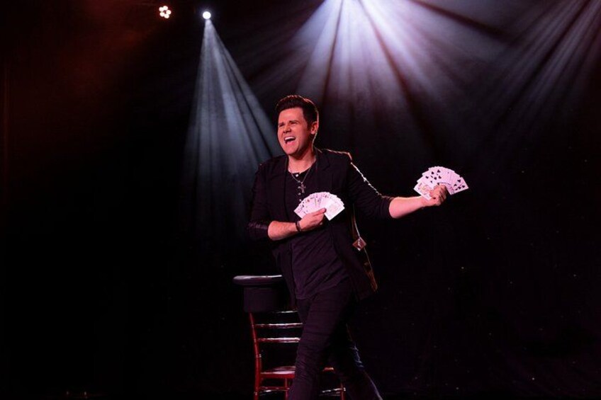 A person on a stage with a spotlight, holding playing cards. 4