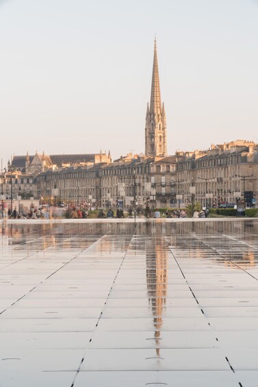 A cathedral with a spire, a reflective plaza, and historic buildings in the background. 1