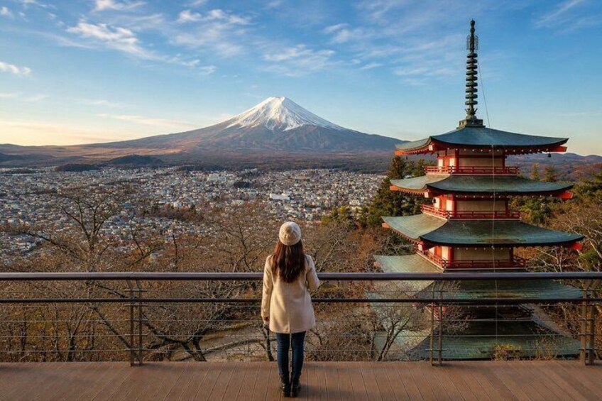 A person standing on a wooden deck overlooking a cityscape with a pagoda and Mount Fuji in the background. 5