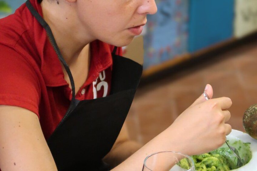 A person wearing a red shirt and black apron, holding a spoon over a bowl of food. 1