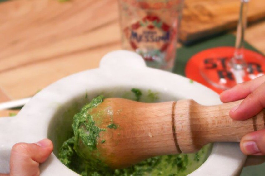 A person using a wooden pestle to grind green herbs in a white mortar. 5