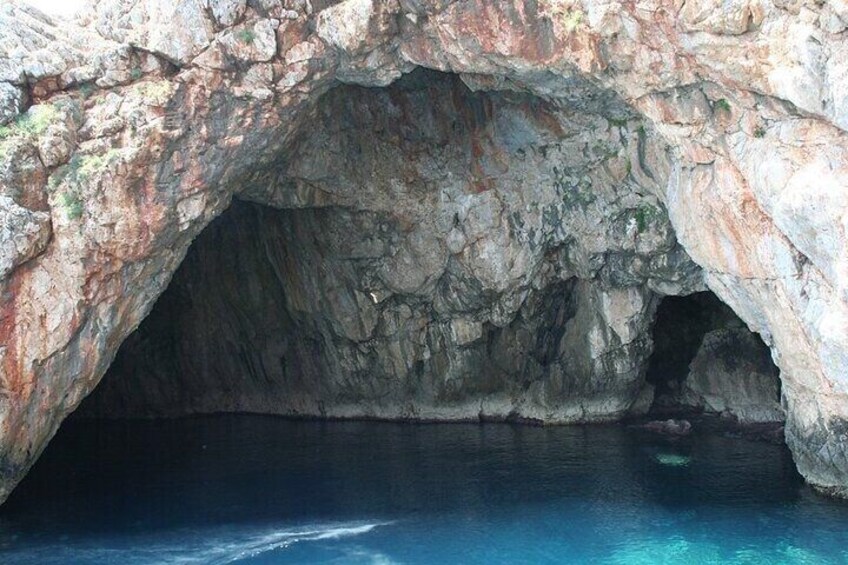 A natural rock formation with a cave entrance and clear blue water. 5