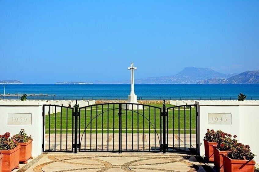 A gated entrance with a cross, a grassy area, and a view of the sea and mountains. 4