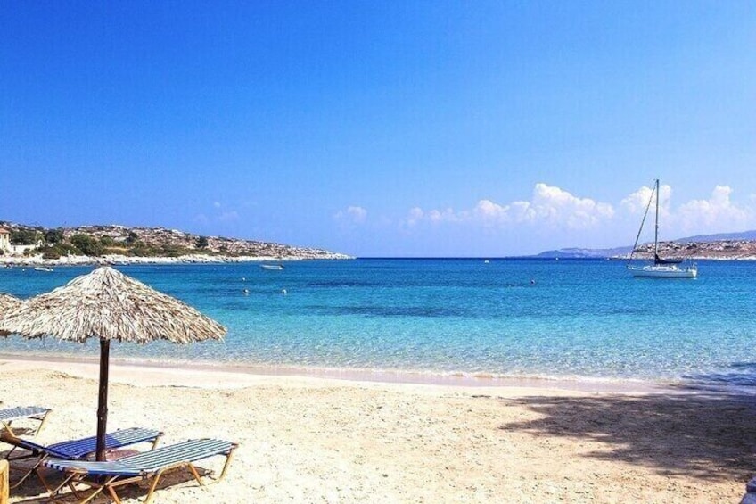 A beach with clear blue water, a sailboat, and lounge chairs. 3