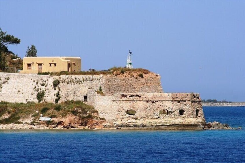 A coastal fortification with a lighthouse, a building on a hill, and a clear blue sea. 2