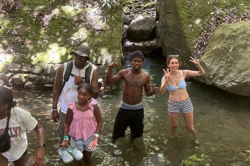 A group of people standing in a shallow stream surrounded by rocks and greenery. 2