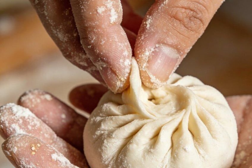 Hands shaping a dumpling with a pleated edge. 1