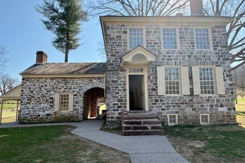 A stone building with a gabled roof, a front door, and a small porch. 2