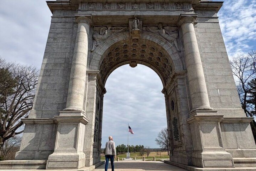 A large stone archway with columns, an American flag, and a person standing in front. 3