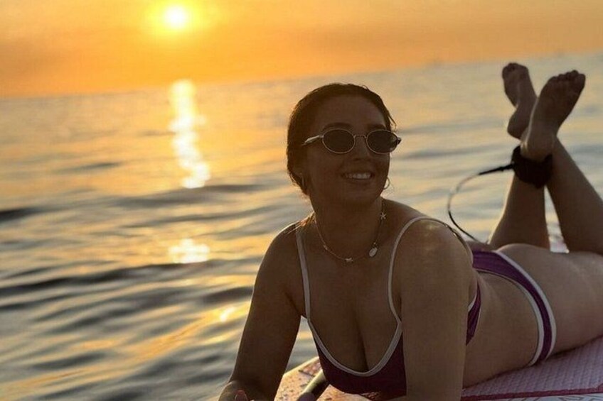A person lying on a beach towel by the water during sunset. 1
