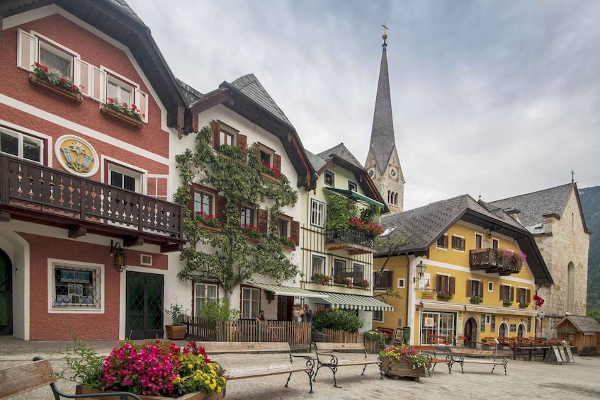 A traditional European town square with colorful buildings, a church steeple, and benches. 2