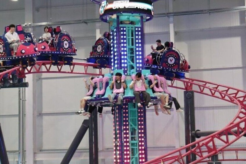 A roller coaster with passengers seated in cars, a central tower structure, and a red track. 3