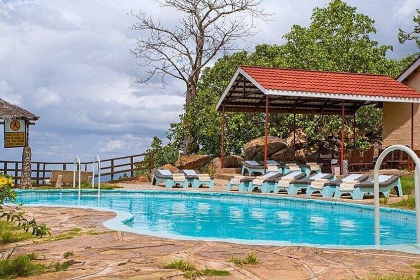 A swimming pool with lounge chairs, a covered seating area, and a natural landscape with trees and rocks. 4