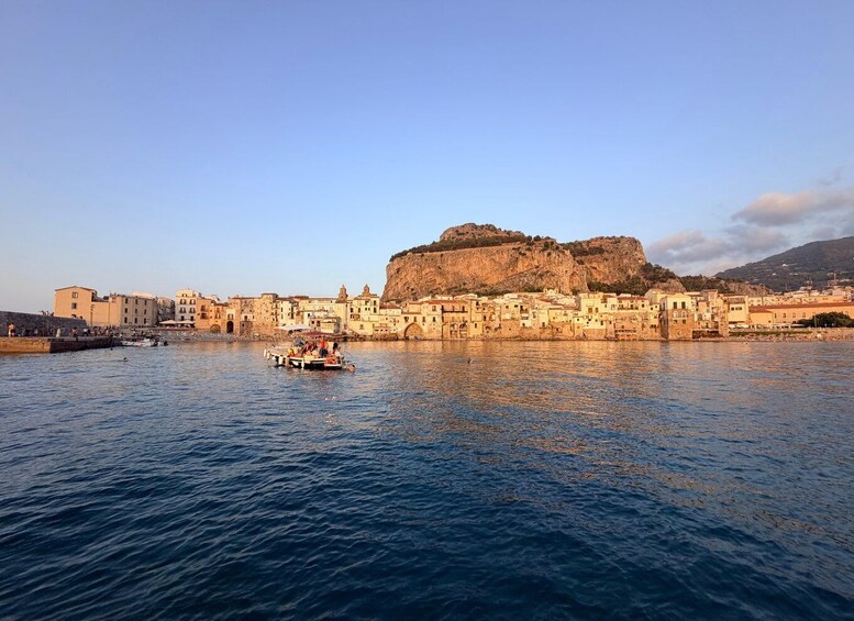A coastal town with buildings along the waterfront, a boat with people on it, and a prominent hill in the background. 3