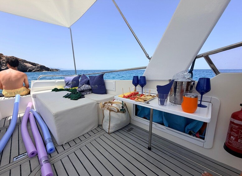 A boat deck with a seating area, a table with snacks and drinks, and a person sitting by the railing. 4