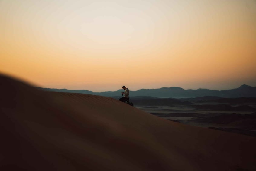 A person climbing a sand dune with a sunset in the background. 2