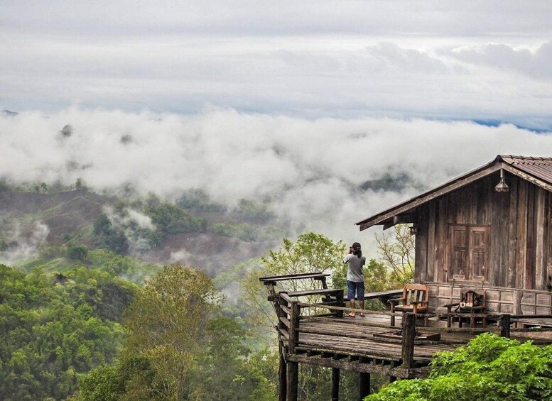 A wooden cabin on a wooden platform overlooking a valley with dense greenery and clouds below. 4