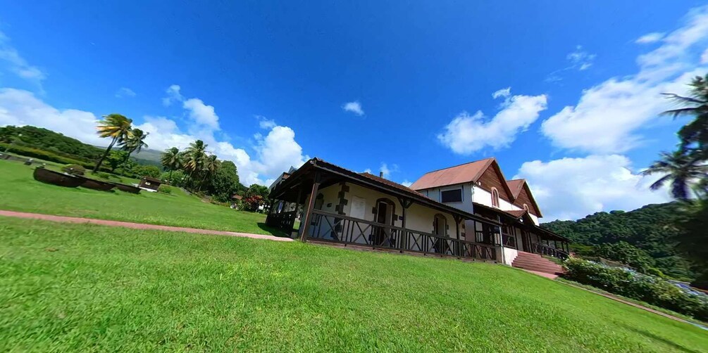 A large house with a red roof and a balcony, surrounded by lush green grass and palm trees. 4